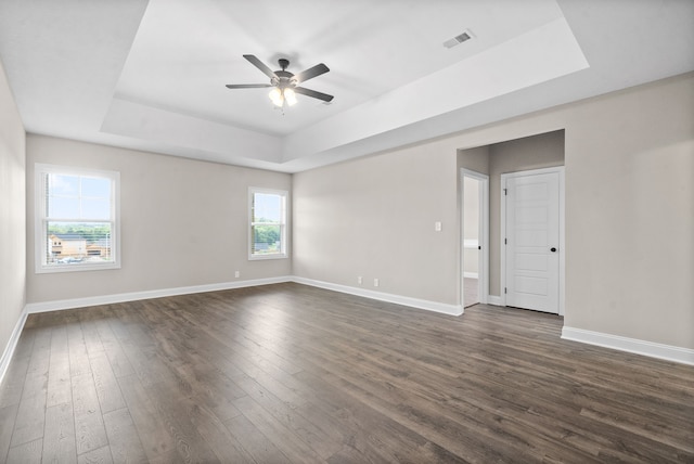 empty room featuring a raised ceiling, ceiling fan, and dark hardwood / wood-style flooring