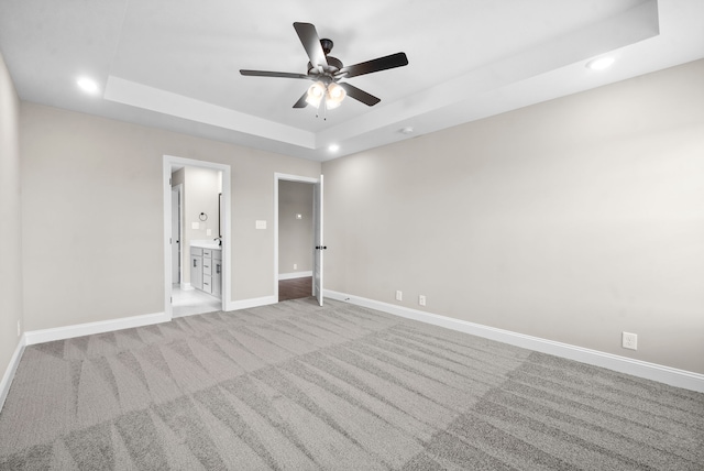 unfurnished bedroom featuring light carpet, connected bathroom, a tray ceiling, and ceiling fan