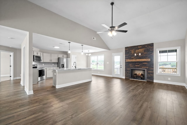 unfurnished living room with sink, a stone fireplace, dark hardwood / wood-style flooring, high vaulted ceiling, and ceiling fan with notable chandelier