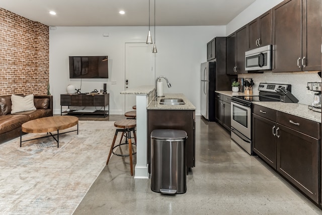 kitchen with appliances with stainless steel finishes, a breakfast bar, light stone countertops, sink, and decorative light fixtures