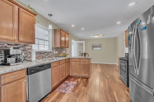 kitchen with sink, light wood-type flooring, kitchen peninsula, hanging light fixtures, and stainless steel appliances