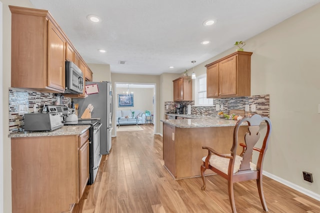 kitchen with kitchen peninsula, appliances with stainless steel finishes, light stone countertops, light hardwood / wood-style flooring, and pendant lighting