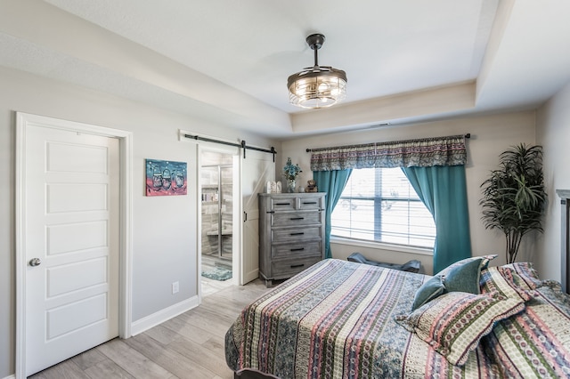 bedroom with a raised ceiling, light wood-type flooring, and a barn door