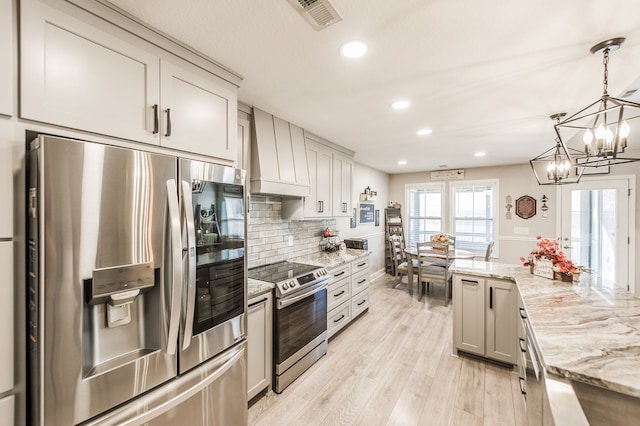 kitchen featuring light wood-type flooring, custom range hood, stainless steel appliances, pendant lighting, and light stone counters