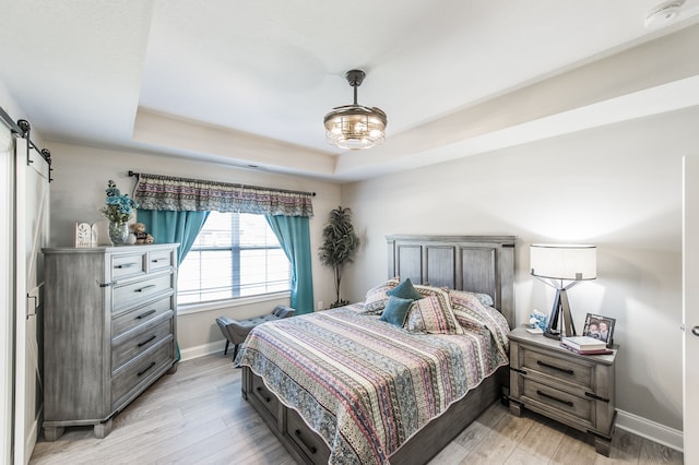 bedroom featuring light hardwood / wood-style floors, a barn door, and a raised ceiling