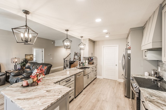 kitchen with light stone countertops, sink, stainless steel appliances, decorative light fixtures, and light hardwood / wood-style flooring