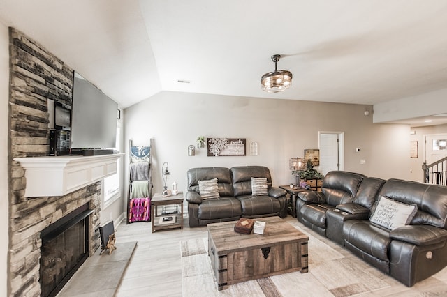 living room featuring lofted ceiling, a stone fireplace, and light hardwood / wood-style floors