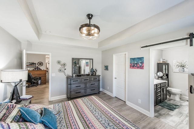 living area with light hardwood / wood-style flooring, a barn door, and a tray ceiling