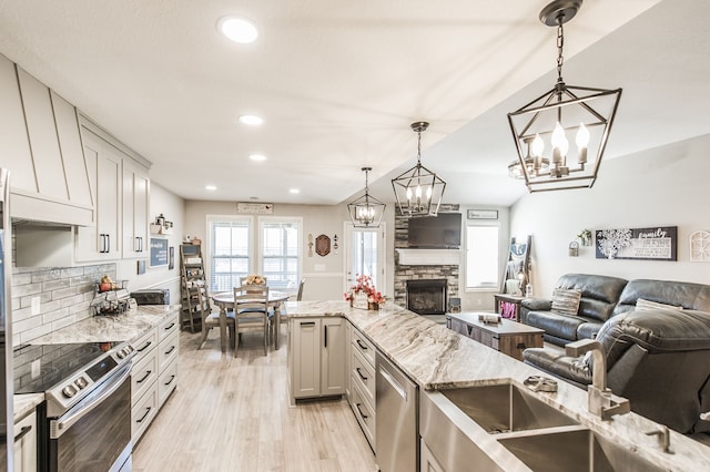 kitchen with light wood-type flooring, a stone fireplace, stainless steel appliances, decorative light fixtures, and light stone counters