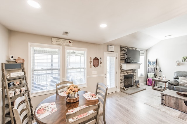 dining room with light hardwood / wood-style floors, lofted ceiling, and a fireplace