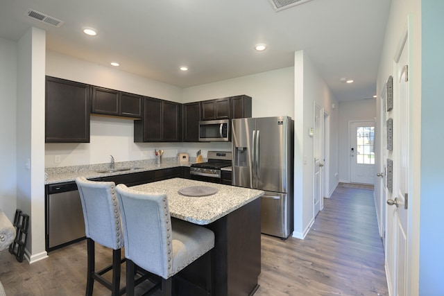 kitchen with appliances with stainless steel finishes, a center island, a kitchen breakfast bar, hardwood / wood-style floors, and light stone counters