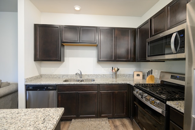 kitchen with dark brown cabinets, light stone countertops, sink, light hardwood / wood-style floors, and stainless steel appliances