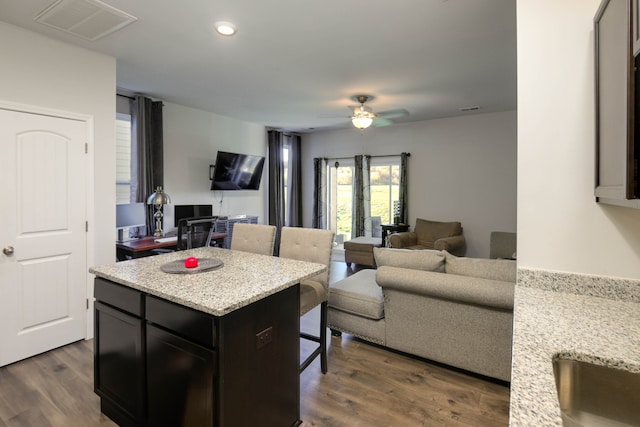 kitchen featuring ceiling fan, light stone countertops, a kitchen island, and dark hardwood / wood-style floors