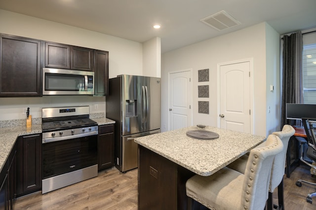 kitchen with a kitchen island, appliances with stainless steel finishes, a kitchen breakfast bar, light hardwood / wood-style flooring, and light stone counters