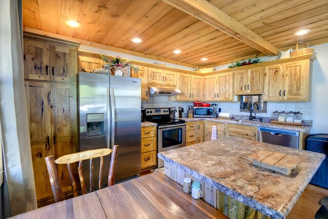 kitchen featuring appliances with stainless steel finishes, sink, backsplash, a center island, and light stone counters