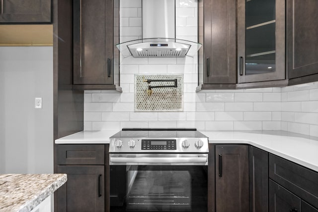 kitchen with dark brown cabinetry, stainless steel electric range, wall chimney range hood, and backsplash