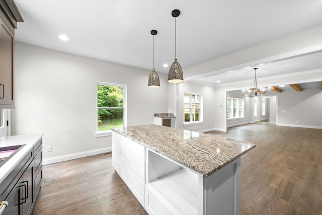 kitchen with dark wood-type flooring, decorative light fixtures, and light stone counters