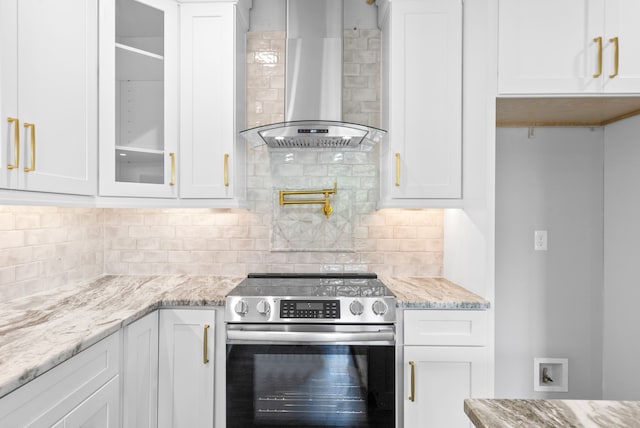 kitchen with stainless steel stove, wall chimney exhaust hood, white cabinets, and light stone countertops