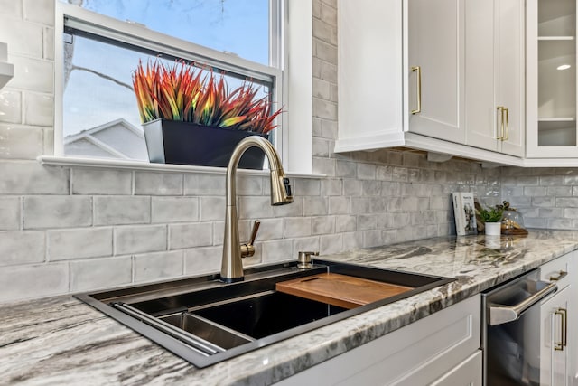 kitchen featuring light stone countertops, white cabinetry, sink, and tasteful backsplash