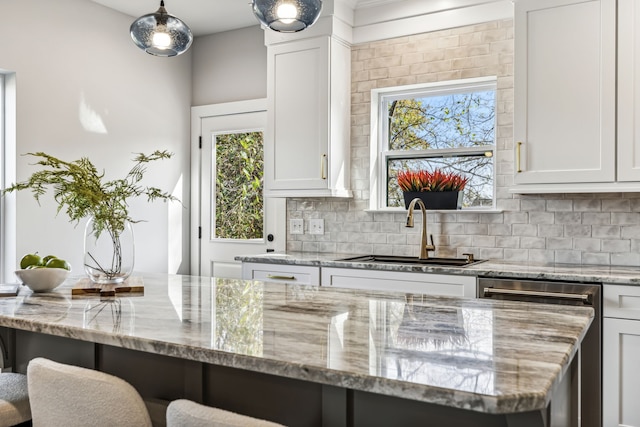 kitchen featuring light stone counters, backsplash, white cabinetry, hanging light fixtures, and sink