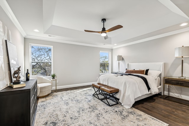 bedroom featuring dark wood-type flooring, multiple windows, ceiling fan, and a raised ceiling