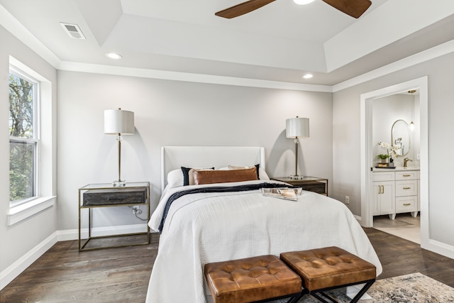 bedroom with connected bathroom, a tray ceiling, ceiling fan, and dark hardwood / wood-style floors