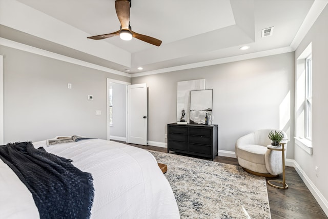 bedroom with dark hardwood / wood-style flooring, ceiling fan, and a tray ceiling