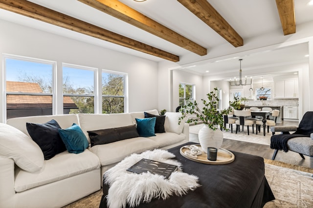 living room featuring light wood-type flooring, crown molding, beam ceiling, and an inviting chandelier