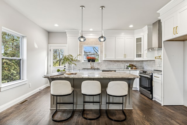 kitchen with white cabinets, stainless steel range with electric stovetop, a center island, and wall chimney range hood