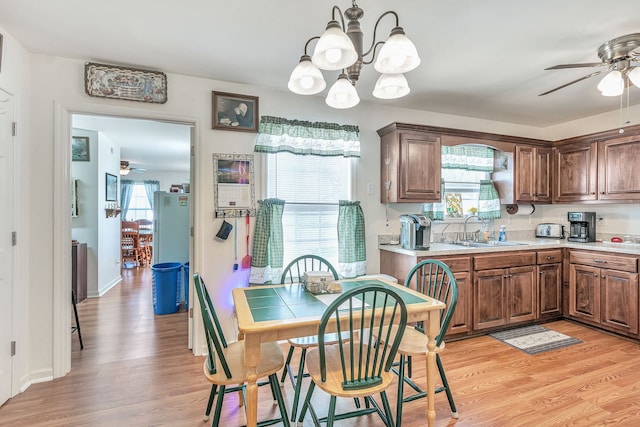 dining area with sink, light hardwood / wood-style flooring, ceiling fan with notable chandelier, and a healthy amount of sunlight