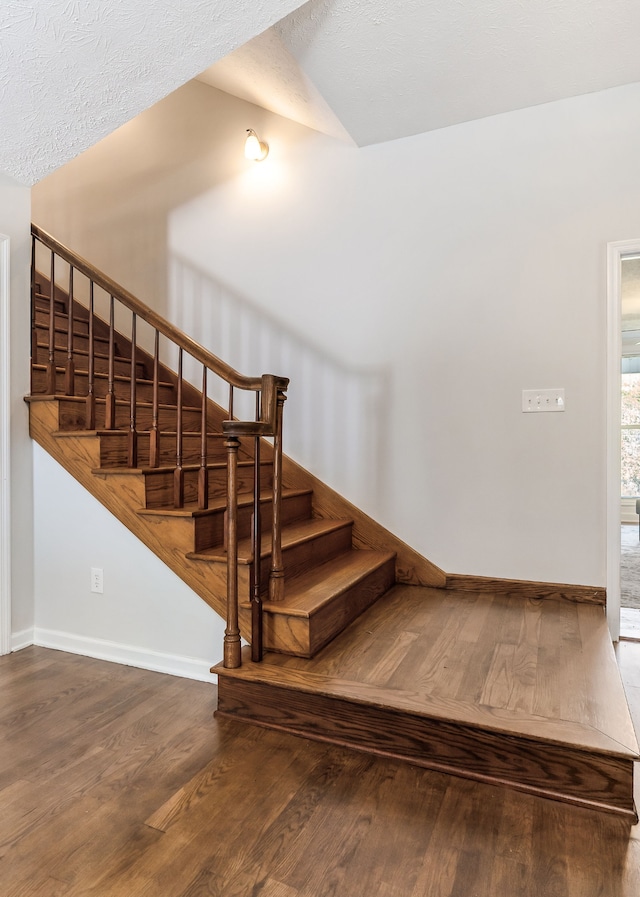 stairs featuring lofted ceiling, a textured ceiling, and hardwood / wood-style flooring