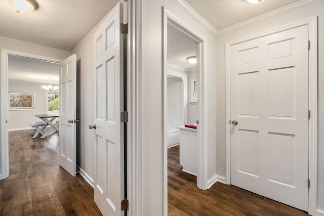 hallway with a textured ceiling, dark hardwood / wood-style flooring, a chandelier, and ornamental molding