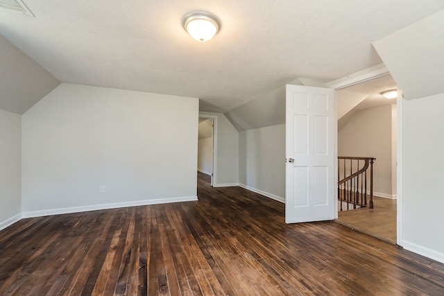 additional living space featuring a textured ceiling, vaulted ceiling, and dark hardwood / wood-style flooring