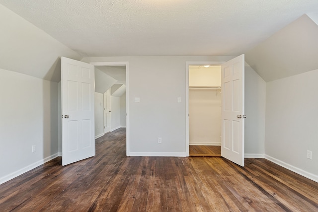 unfurnished bedroom with a textured ceiling, a spacious closet, vaulted ceiling, dark wood-type flooring, and a closet