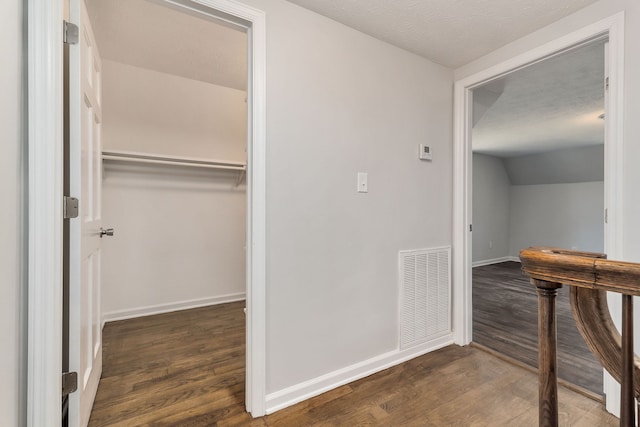 hallway featuring dark wood-type flooring, vaulted ceiling, and a textured ceiling