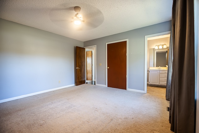 unfurnished bedroom with ceiling fan, a textured ceiling, sink, ensuite bath, and light colored carpet