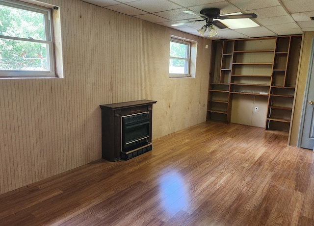 unfurnished living room featuring a paneled ceiling, hardwood / wood-style flooring, ceiling fan, and wood walls