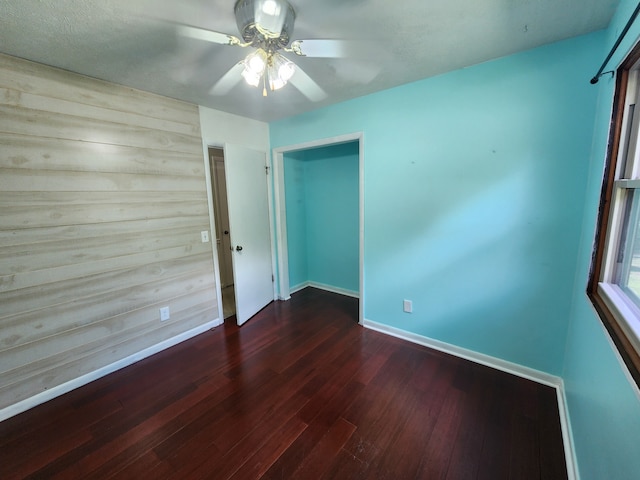 spare room featuring ceiling fan, dark wood-type flooring, and wood walls