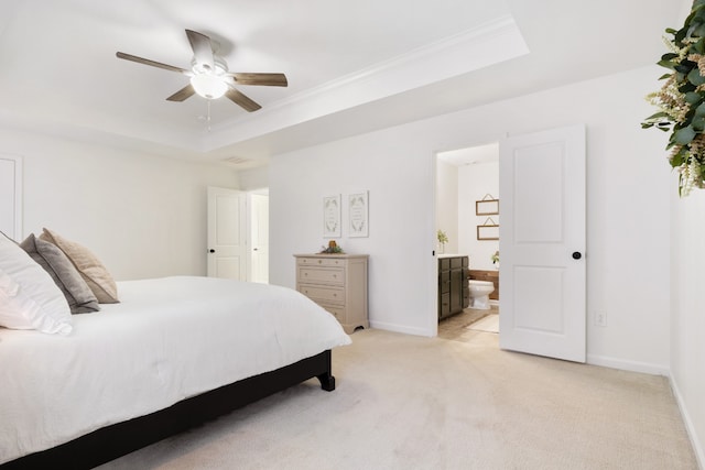 bedroom featuring connected bathroom, light carpet, a tray ceiling, and ceiling fan