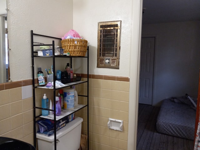 interior space with tile walls, heating unit, and toilet