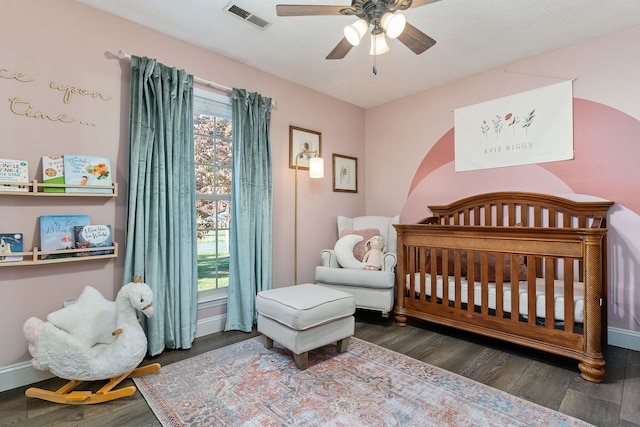 bedroom featuring a nursery area, ceiling fan, and dark hardwood / wood-style floors