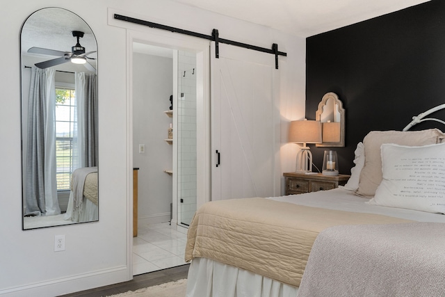 bedroom featuring ensuite bath, a barn door, hardwood / wood-style flooring, and ceiling fan