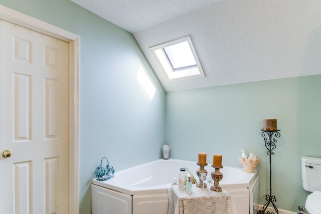 bathroom featuring vaulted ceiling with skylight, a textured ceiling, toilet, and a bathing tub