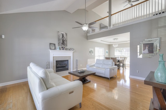 living room with beam ceiling, ceiling fan, high vaulted ceiling, light wood-type flooring, and a fireplace