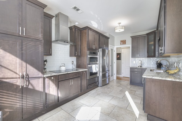 kitchen featuring light stone countertops, stainless steel appliances, wall chimney exhaust hood, and sink