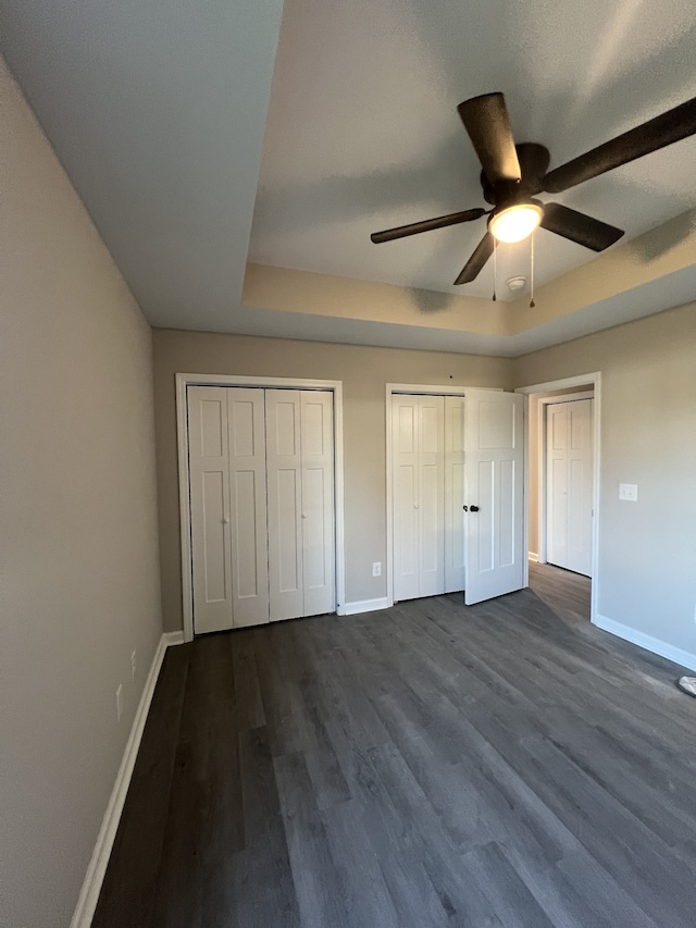 unfurnished bedroom with hardwood / wood-style floors, multiple closets, a tray ceiling, and ceiling fan