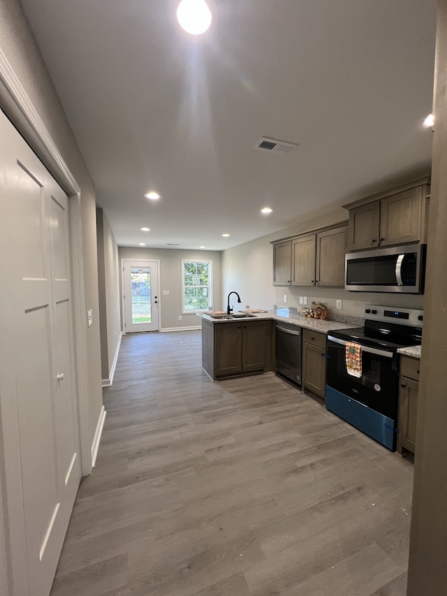 kitchen with kitchen peninsula, stainless steel appliances, sink, and light wood-type flooring