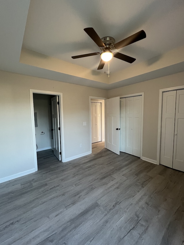 unfurnished bedroom featuring ceiling fan, multiple closets, a tray ceiling, and light hardwood / wood-style floors