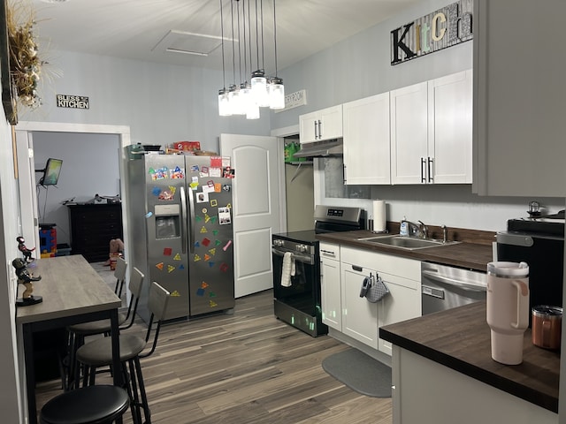 kitchen with appliances with stainless steel finishes, white cabinetry, pendant lighting, wooden counters, and sink