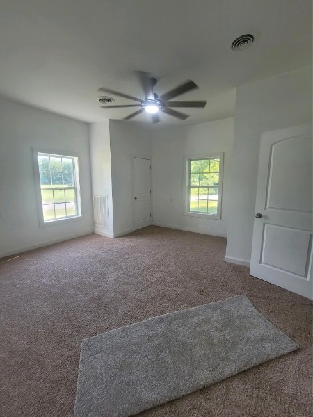 unfurnished room with ceiling fan, carpet flooring, and a wealth of natural light